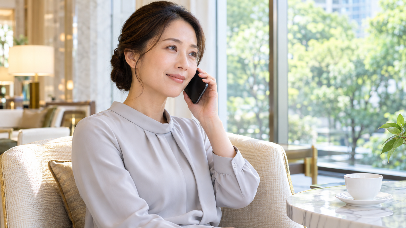 明るい窓辺の椅子に座りスマートフォンで話す女性