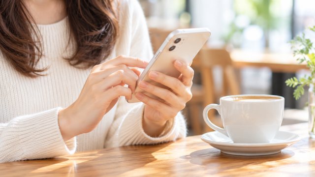 カフェでスマートフォンからメッセージを送る女性の手元