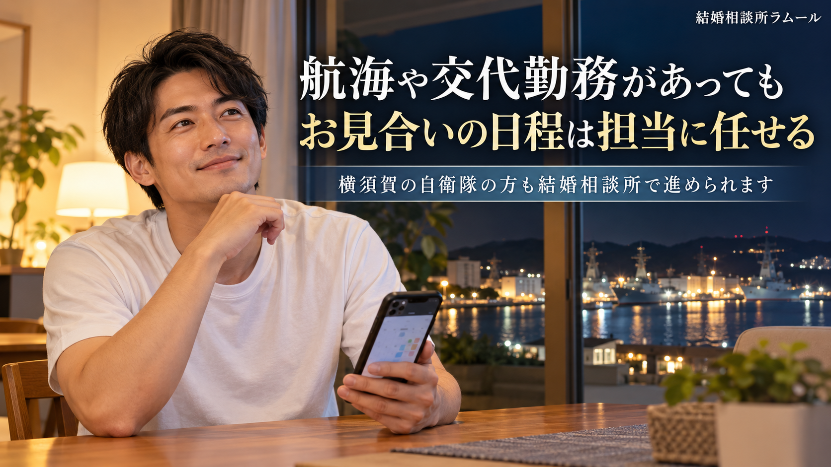 夜の自宅のダイニングでスマートフォンを手に顔を上げて微笑む白いTシャツの33歳の男性(航海や交代勤務があってもお見合いの日程は担当に任せる・横須賀の自衛隊の方も結婚相談所で進められる)